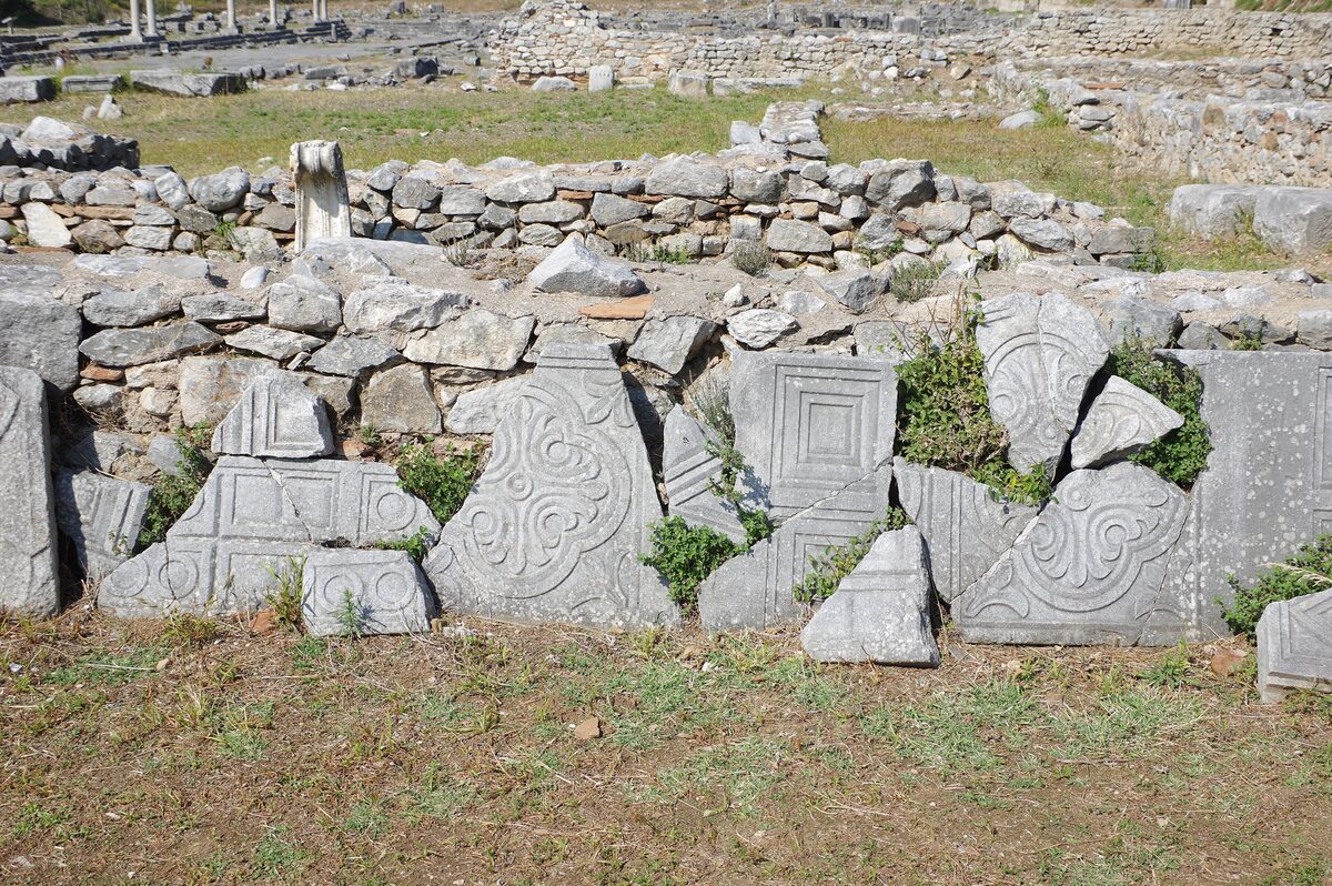 Carved marble blocks and ruined walls lying in the grass at the archaeological site of Philippi