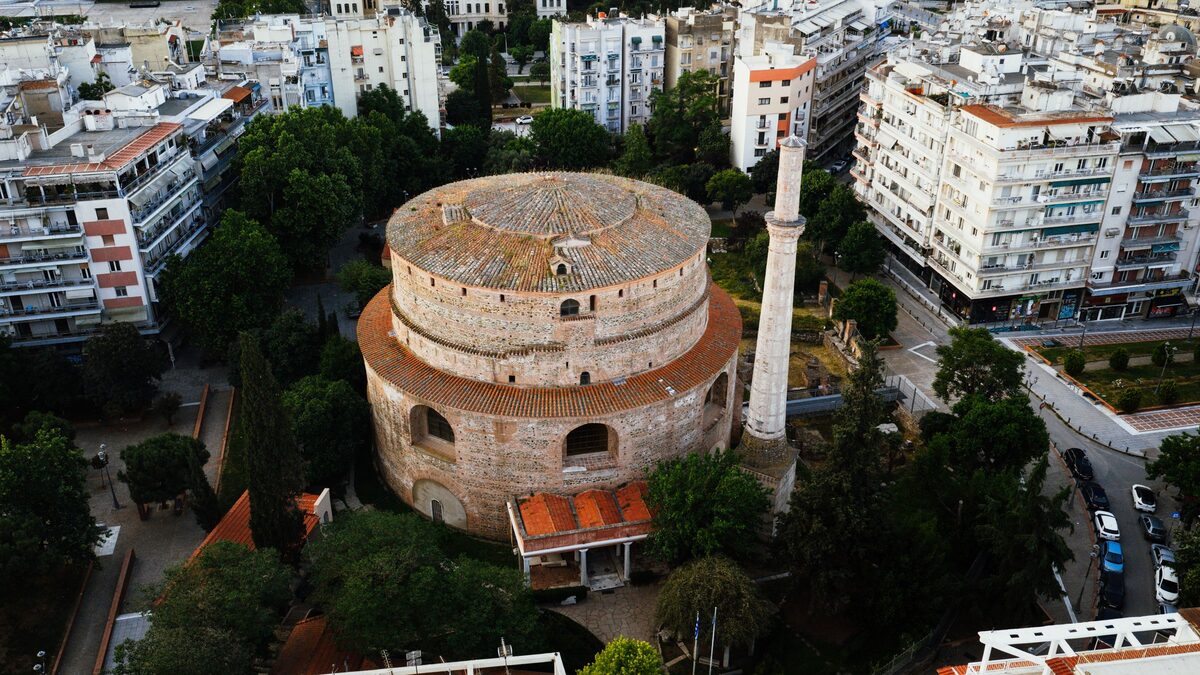 The round brick Rotunda of Thessaloniki seen from above, with its tiled dome, the tall white Ottoman minaret beside it and apartment blocks all around