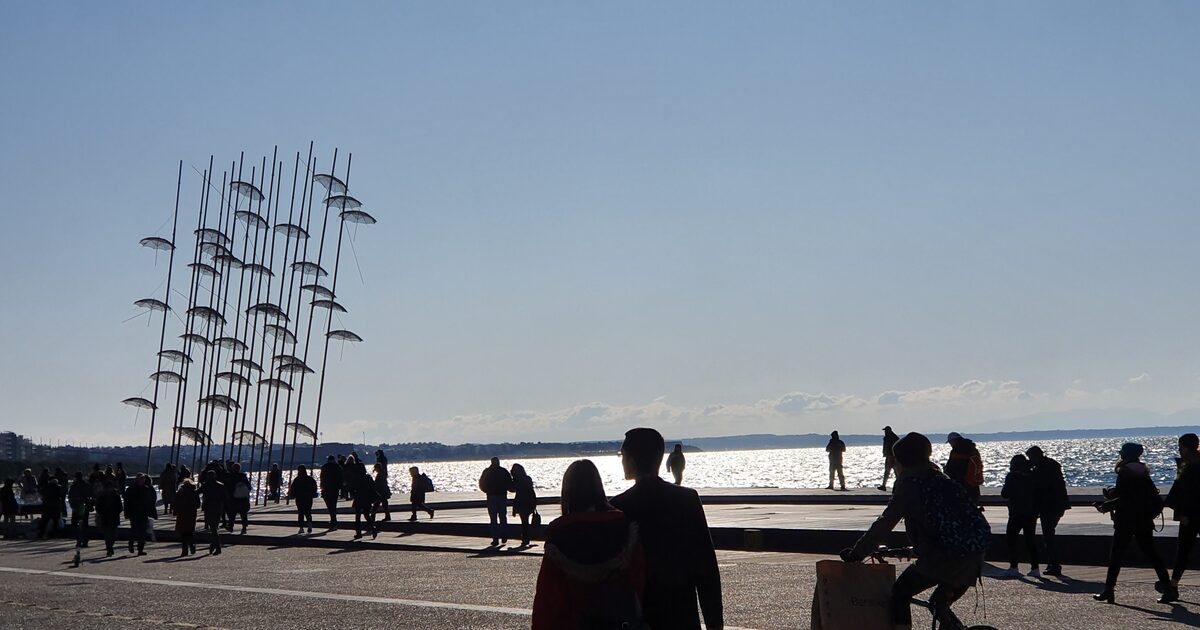 The Umbrellas sculpture, dozens of metal umbrellas on tall poles, silhouetted against the sea with people walking along the promenade