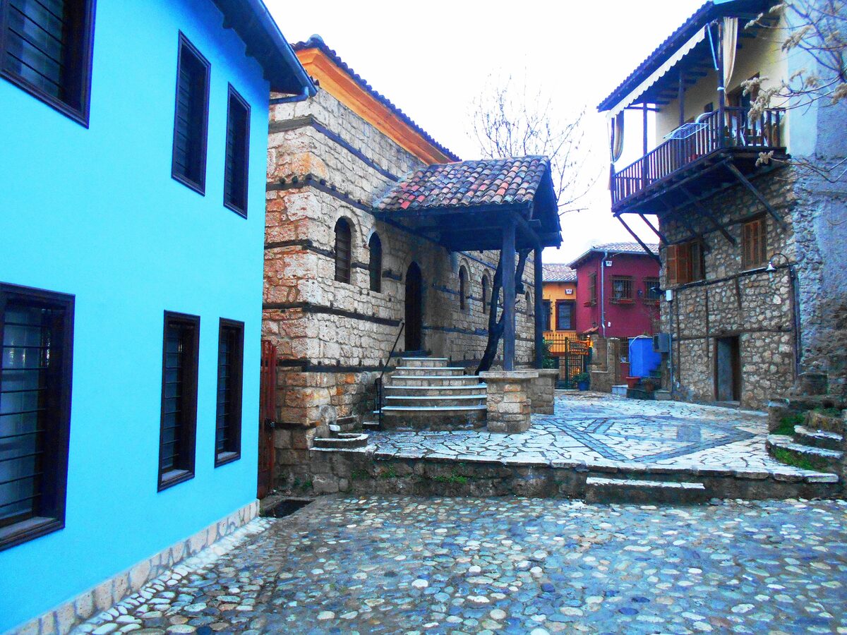A cobbled lane in the Barbouta quarter of Veria with brightly painted old houses, a wooden balcony and a stone building with a tiled porch