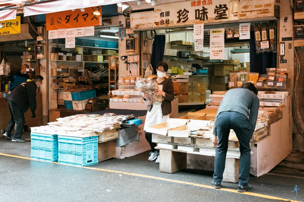 A dried-food and seafood stall in the Ameyoko market in Ueno on a bright day, with crates stacked in front and shoppers at the counter