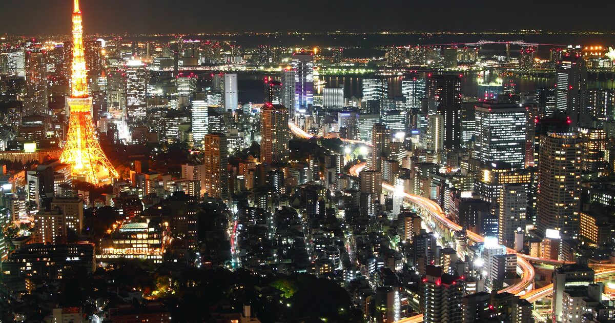 Tokyo Tower lit orange at night among the towers and expressways of the city, with Tokyo Bay on the horizon