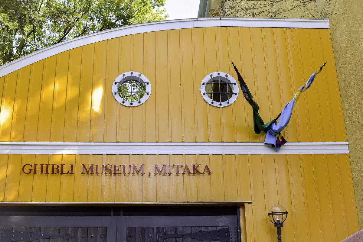 The yellow facade of the Ghibli Museum in Mitaka with its name on the wall and a metal sculpture beside it