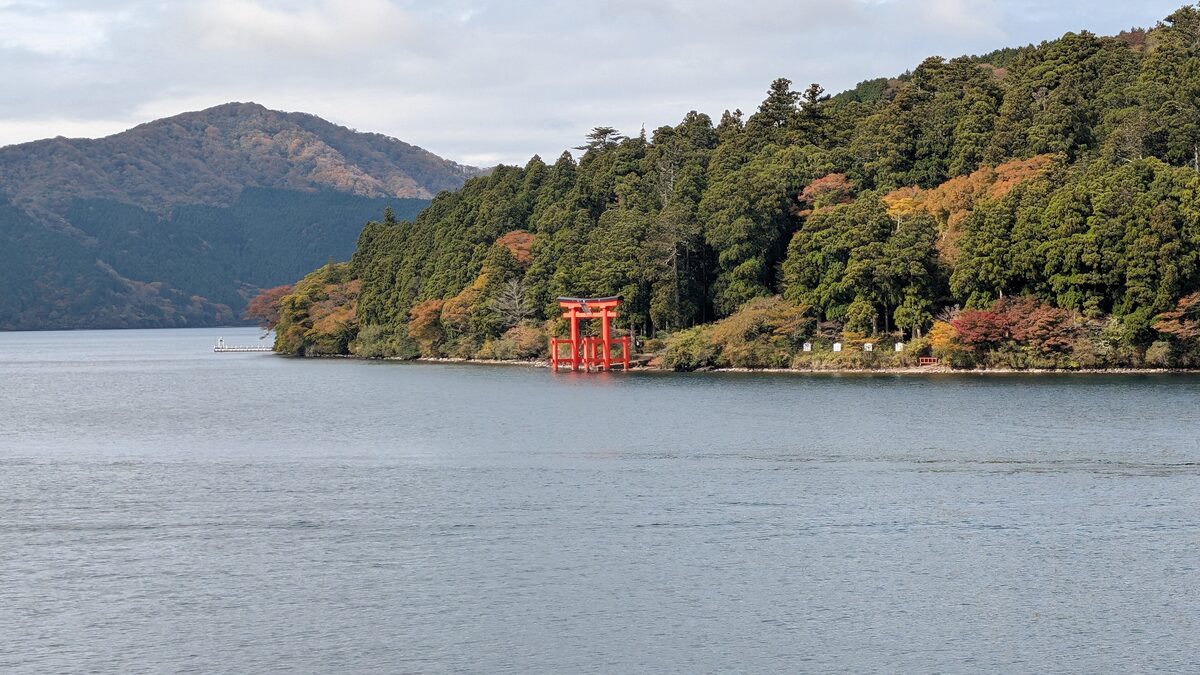 Lake Ashi with a red torii gate on the far shore and wooded hills behind
