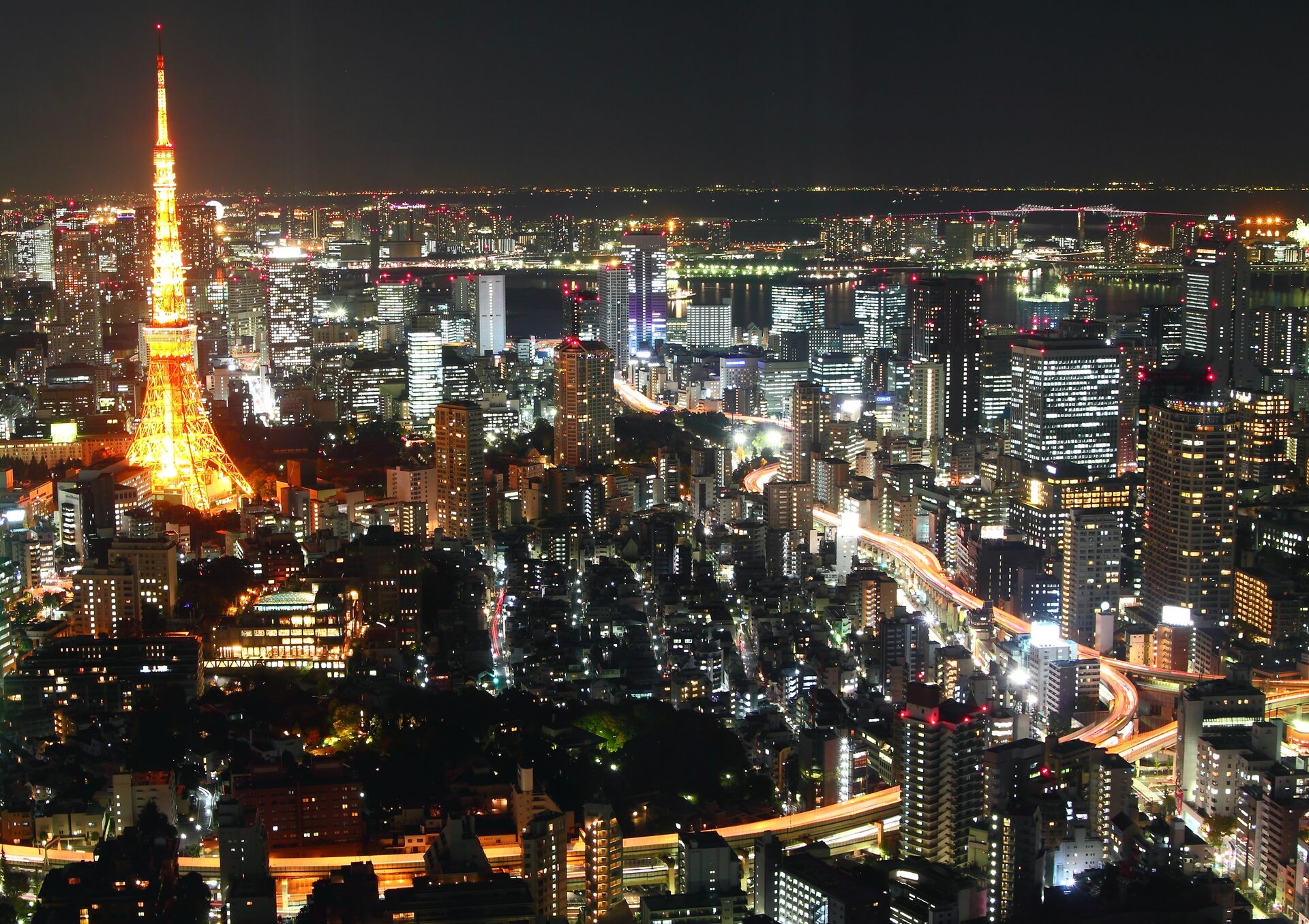 Tokyo Tower lit orange at night among the towers and expressways of the city, with Tokyo Bay on the horizon