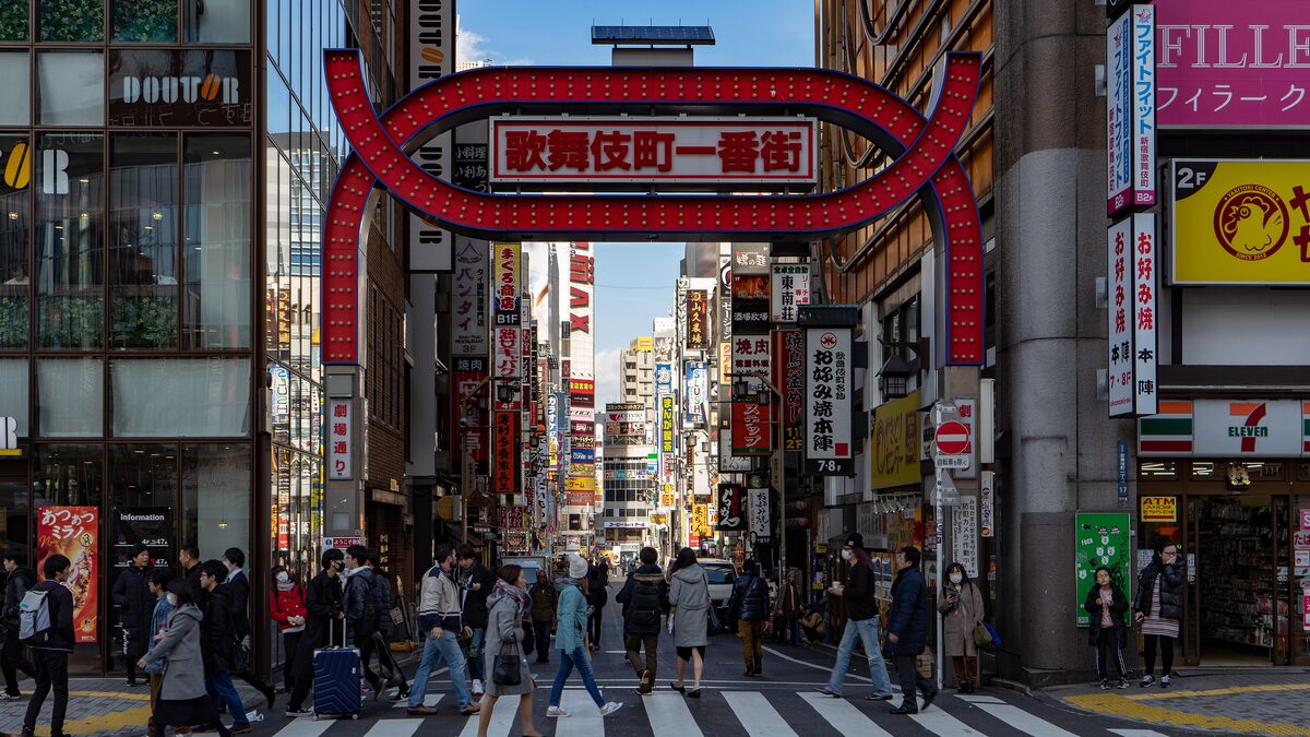 The red Kabukicho Ichiban-gai gate over the main street into Kabukicho in Shinjuku, with signs on both sides and people crossing in the foreground