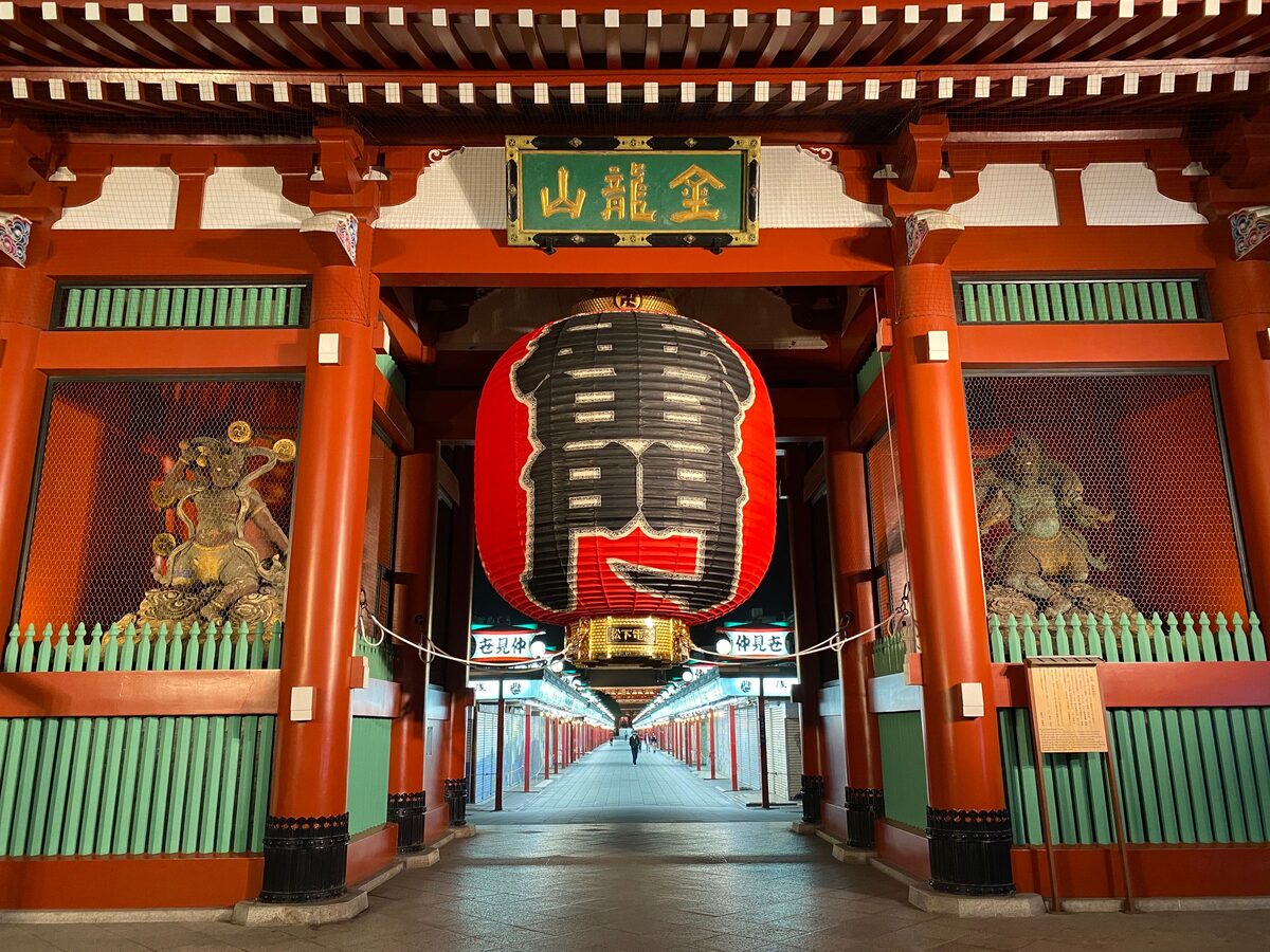 The giant red paper lantern hanging in the Kaminarimon gate, with a guardian statue on each side and the Nakamise shopping street running away behind it