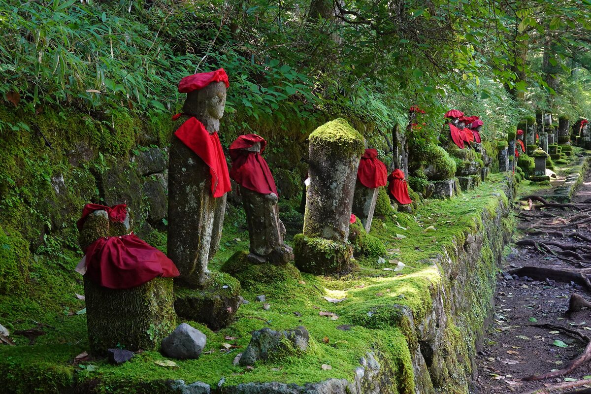 Mossy jizo statues in red bibs beside the path near the Kanmangafuchi Abyss in Nikko