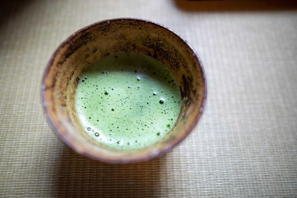 Frothy bright-green matcha in a rustic ceramic bowl on a woven mat