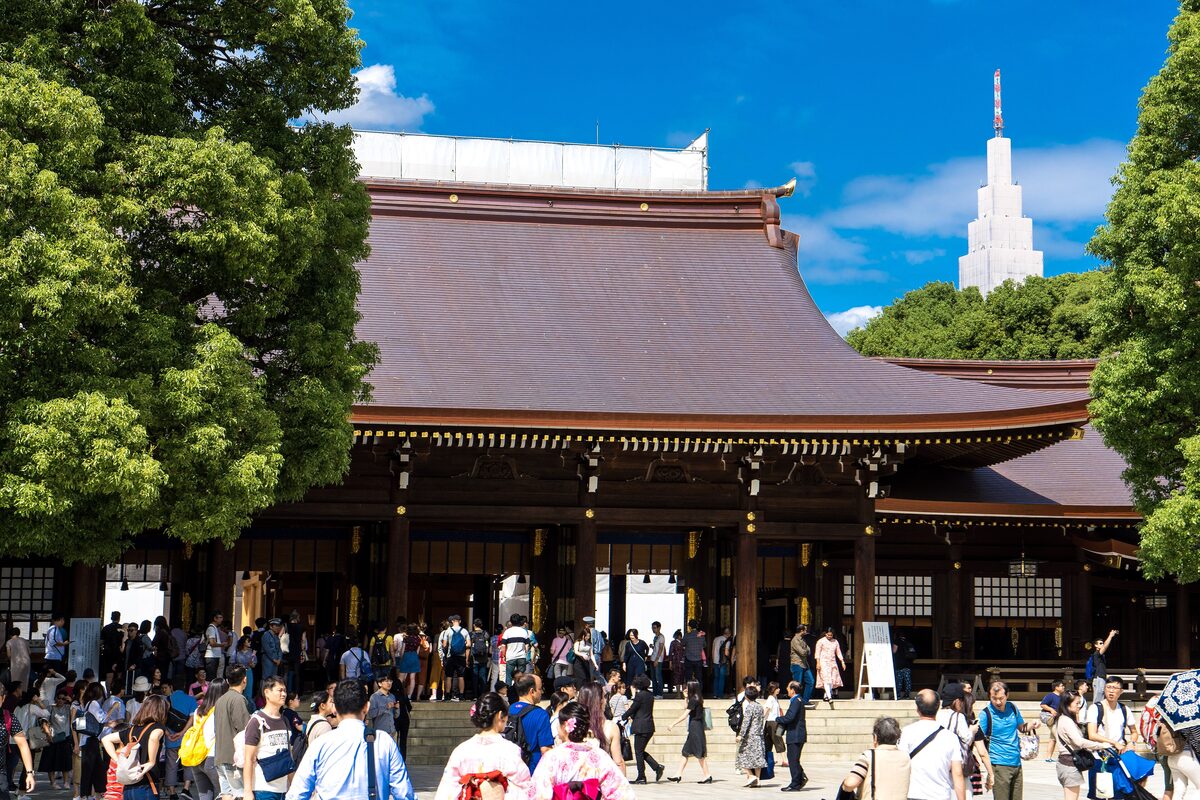 The main hall of Meiji Jingu among tall trees, with visitors on the stone approach