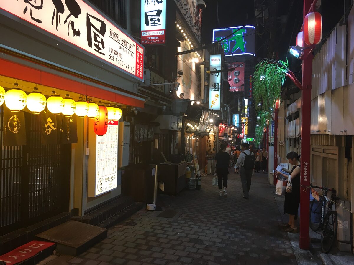 A narrow alley in Omoide Yokocho at night, with yellow lanterns over the small bar fronts and a red lamp post