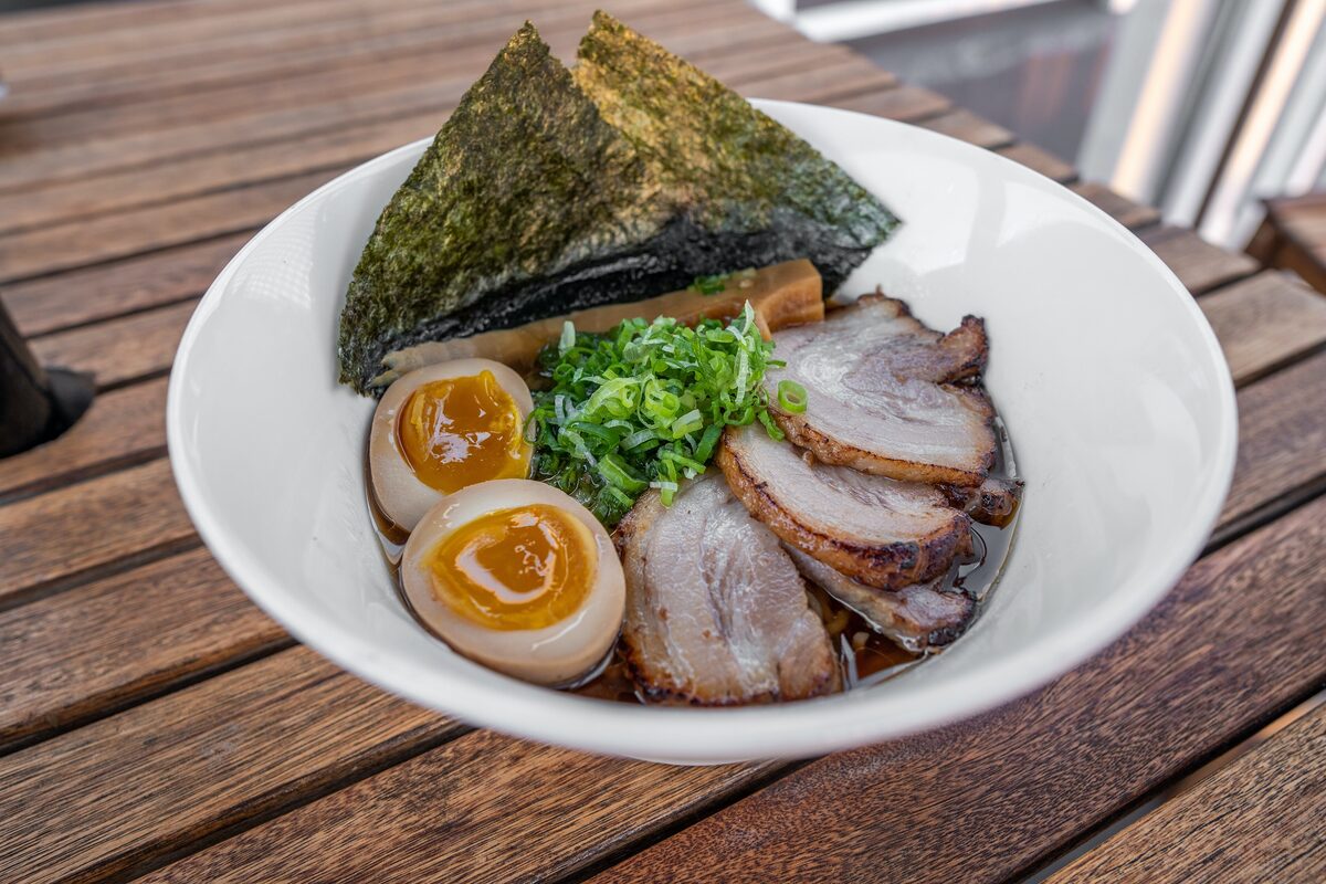 A bowl of ramen topped with chashu pork, a marinated egg, nori and spring onion