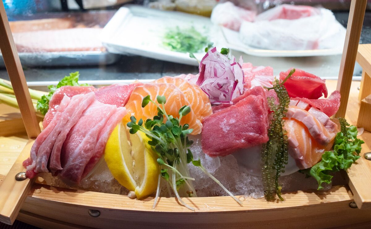 A wooden boat of sashimi on ice with sliced tuna, salmon and other raw fish, a lemon wedge and sprouts