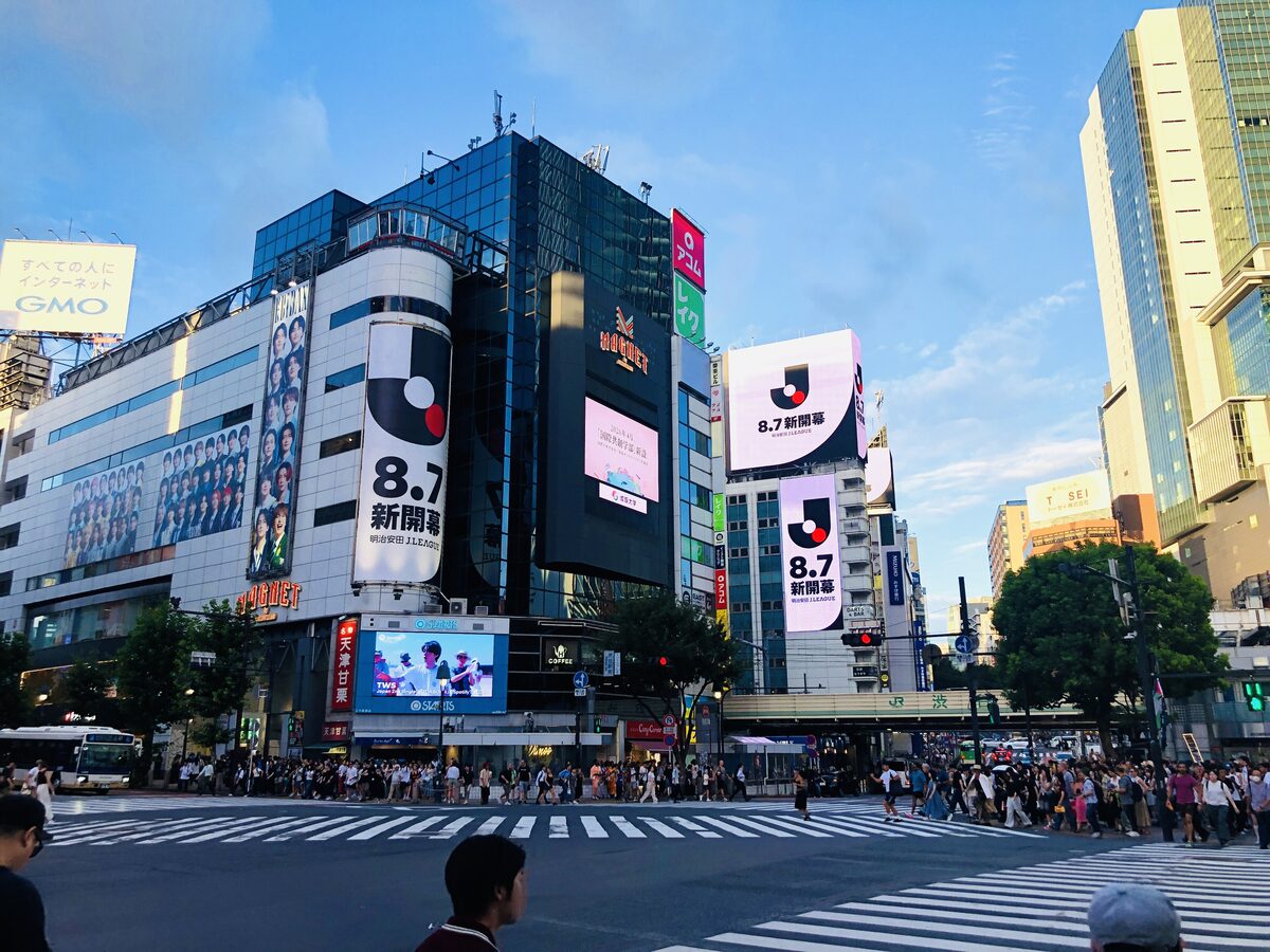 Crowds crossing the Shibuya scramble at street level, with big billboards on the buildings around