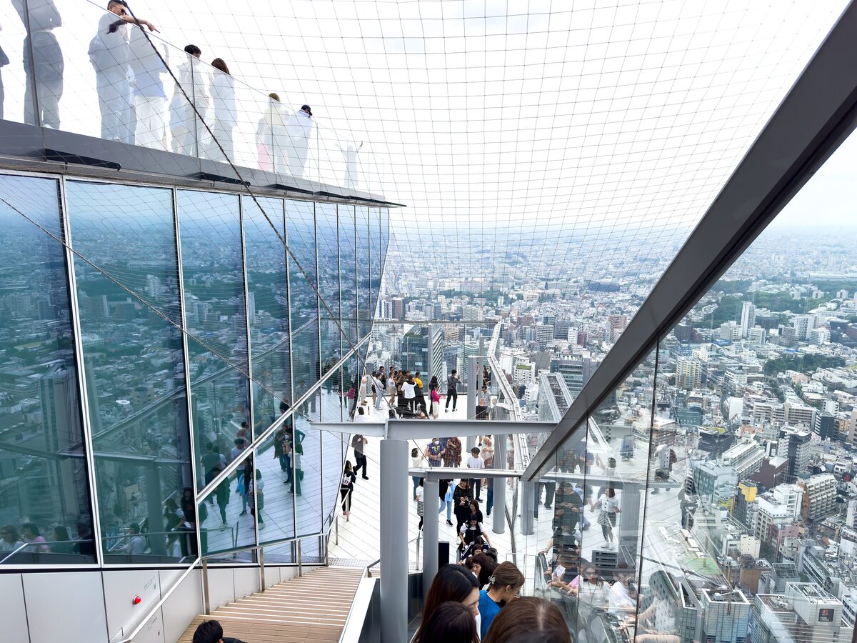 Visitors on the glass-floored open deck of Shibuya Sky with the city spread out below