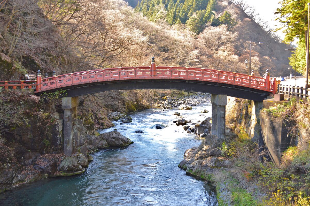 The red Shinkyo bridge spanning the river gorge in Nikko, with wooded hills behind