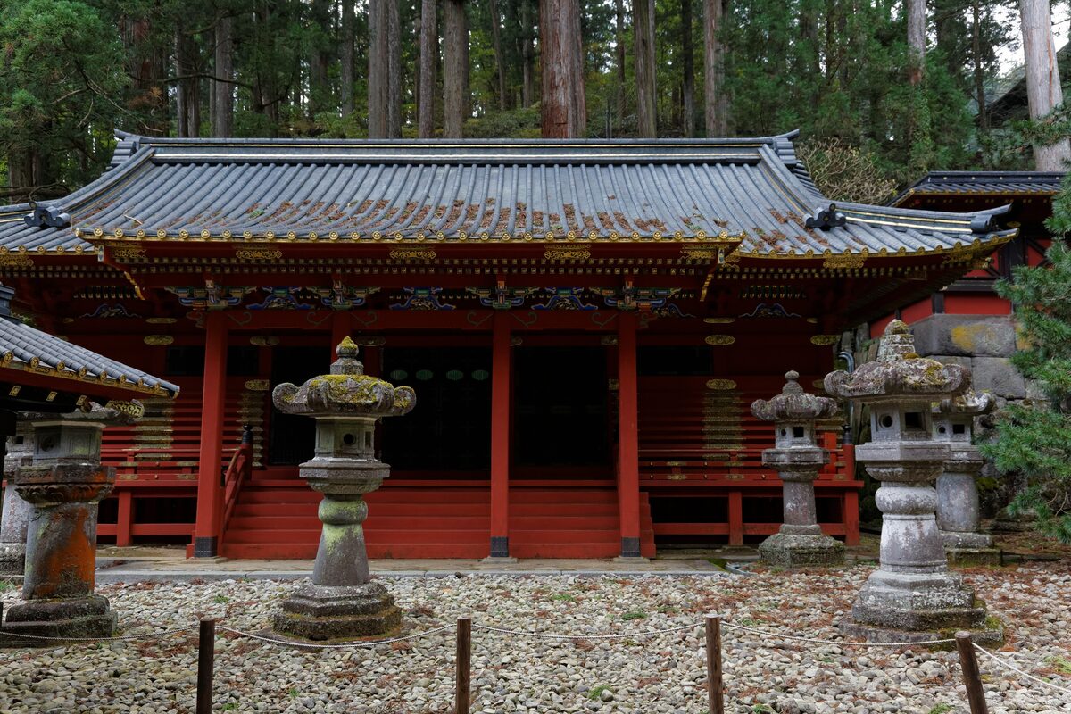 A red-and-gold hall at the Taiyuinbyo mausoleum in Nikko, with stone lanterns in front and cedar forest behind