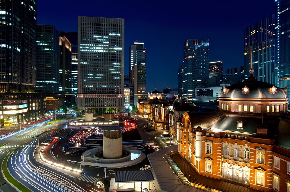 Tokyo Station's red-brick Marunouchi building at night, with light trails from the traffic in front