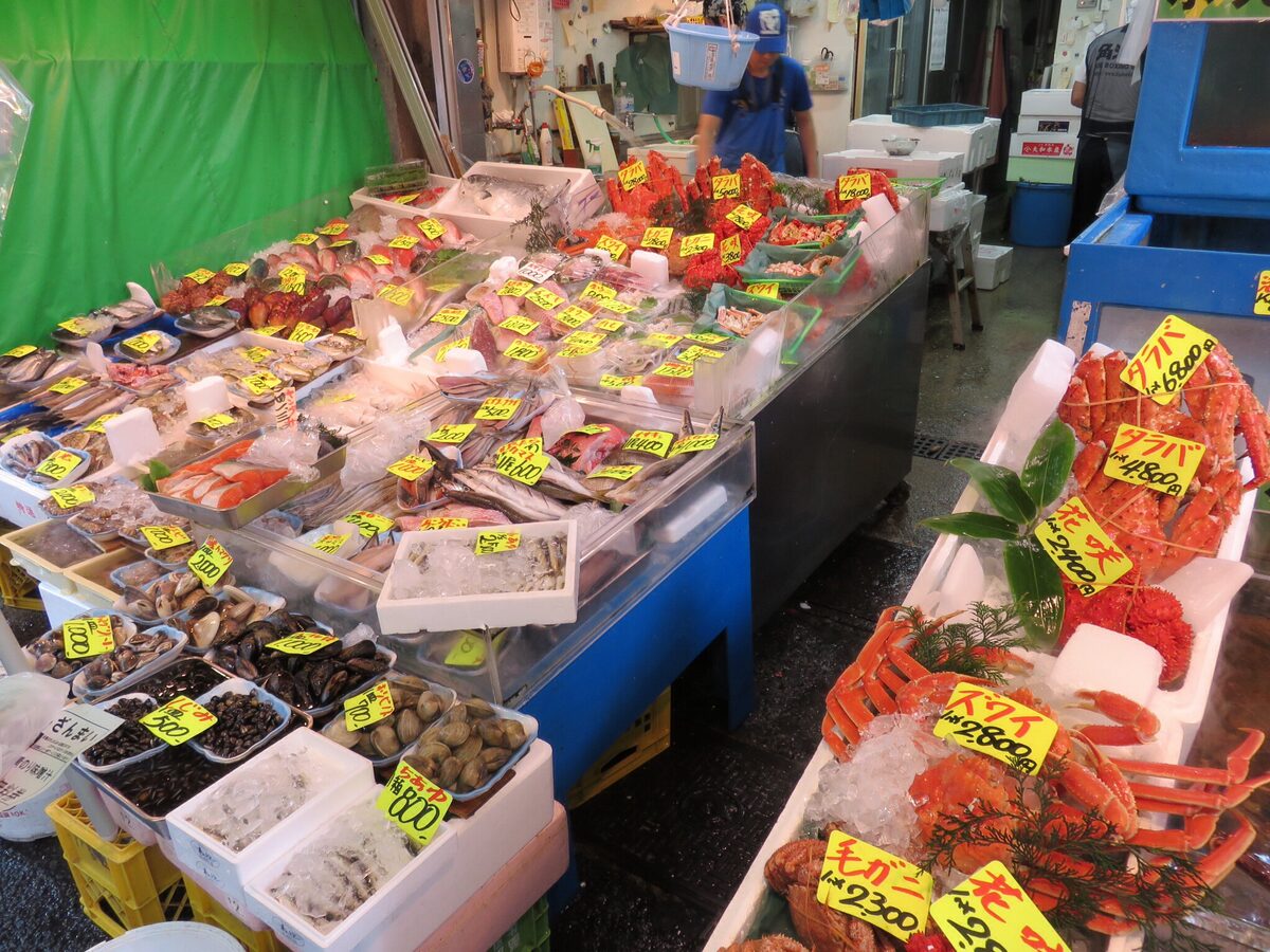 A seafood stall at the Tsukiji Outer Market with crabs, shellfish and sliced fish on ice, each with a yellow price tag