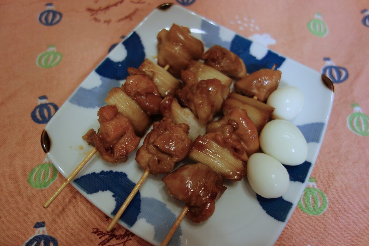 Grilled chicken yakitori skewers on a patterned plate, with boiled quail eggs