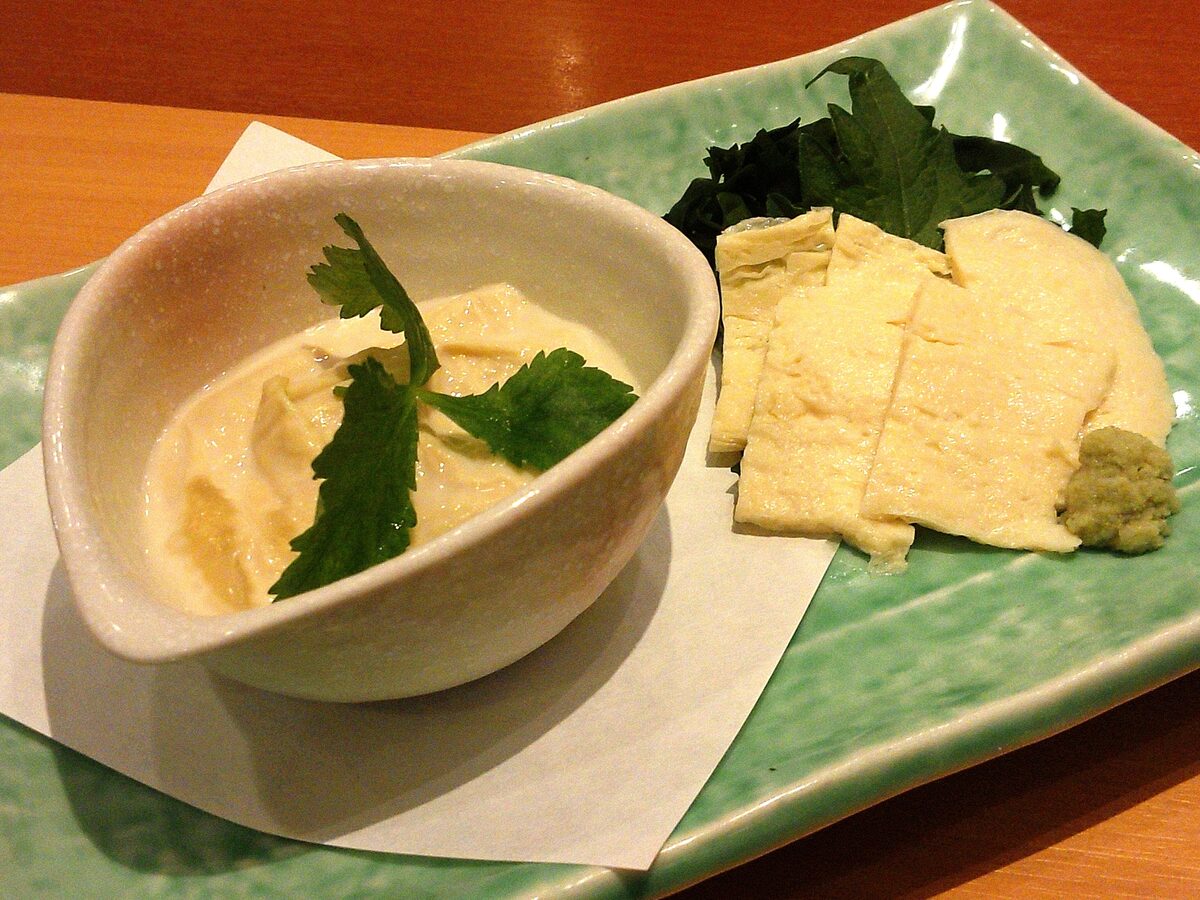 Two kinds of yuba on a green plate: a bowl of fresh, soft tofu skin and sliced sheets served like sashimi with wasabi