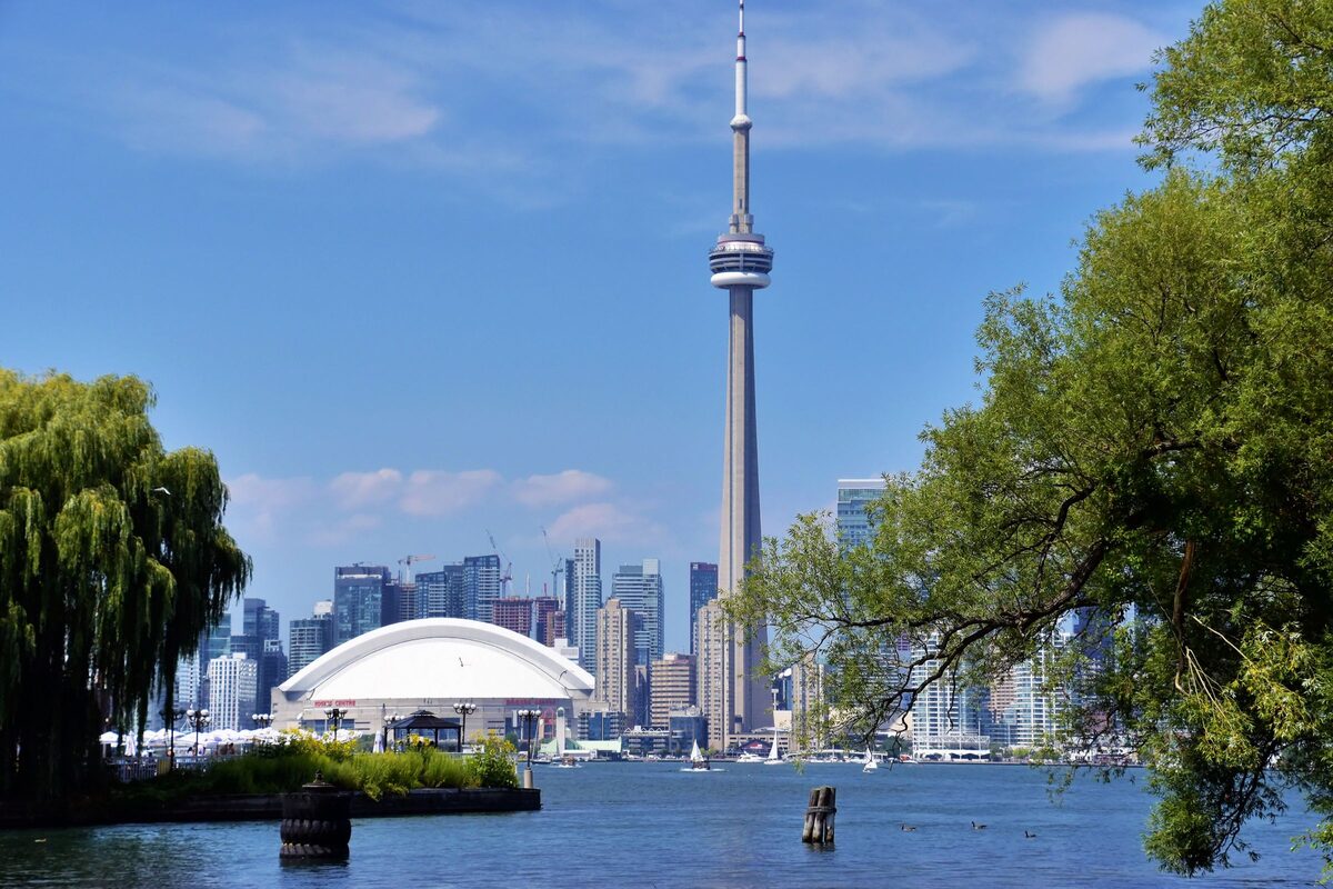 The CN Tower rising above the Toronto waterfront and the white roof of the Rogers Centre, framed by trees