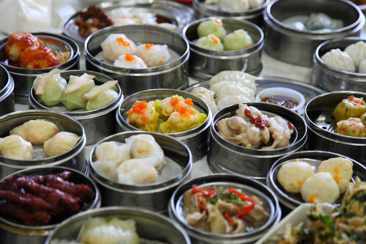 Rows of bamboo steamers and small dishes of dim sum dumplings, rolls and buns