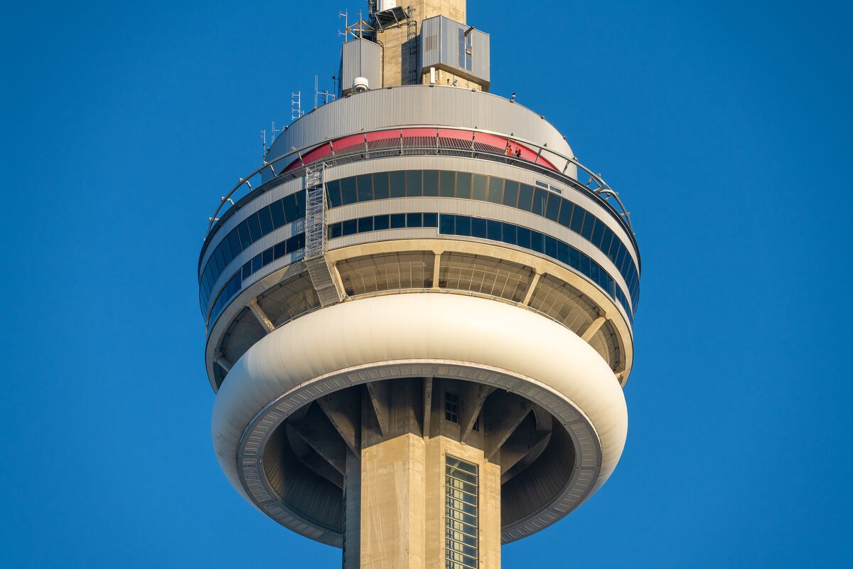 The main pod of the CN Tower against a deep blue sky, with the EdgeWalk ledge around its rim