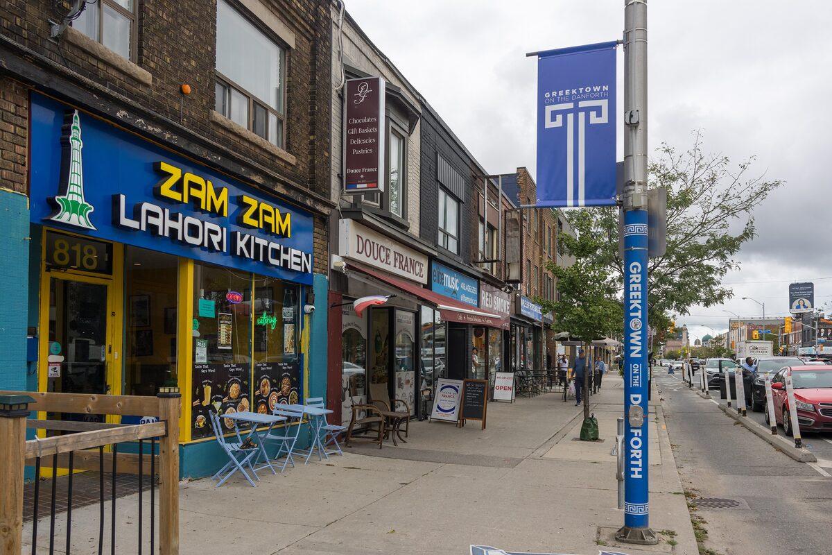 Danforth Avenue shopfronts and cafe tables under a Greektown on the Danforth banner
