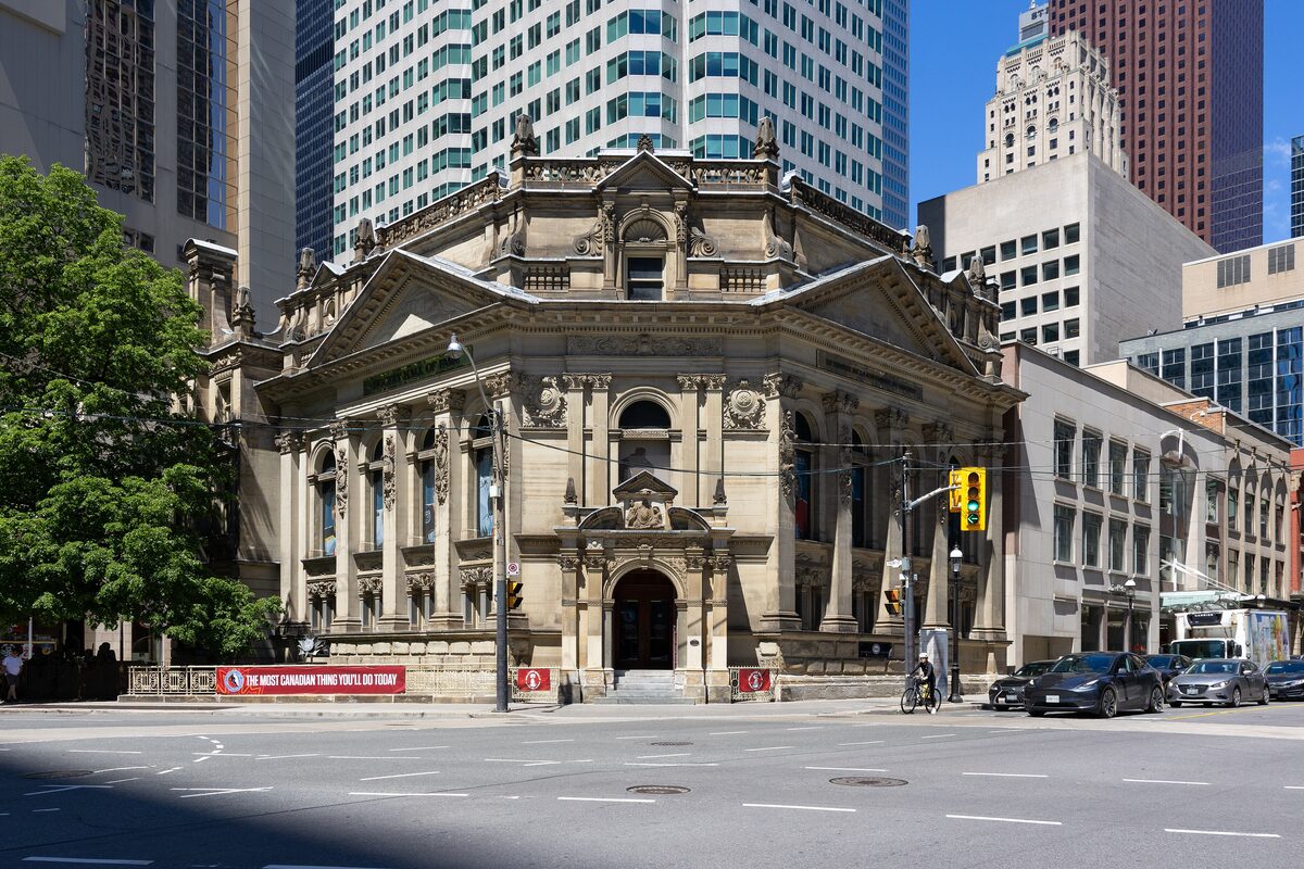 The ornate stone facade of the former Bank of Montreal building that houses the Hockey Hall of Fame, between glass towers