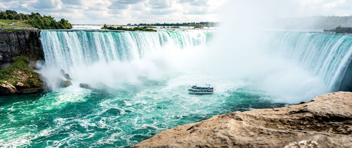 Horseshoe Falls curving into its turquoise gorge with mist rising and a tour boat in the water below