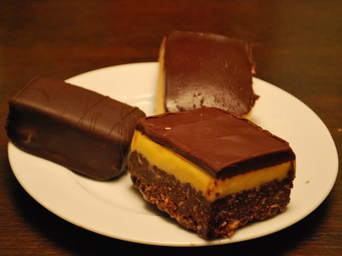 Nanaimo bars on a plate, showing the chocolate top, yellow custard middle and crumb base