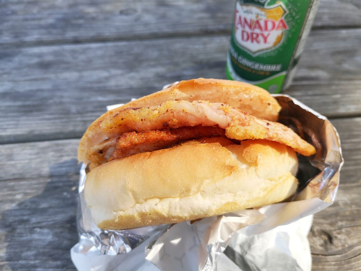 A peameal bacon sandwich on a Kaiser roll from Carousel Bakery in St. Lawrence Market, wrapped in foil beside a ginger ale