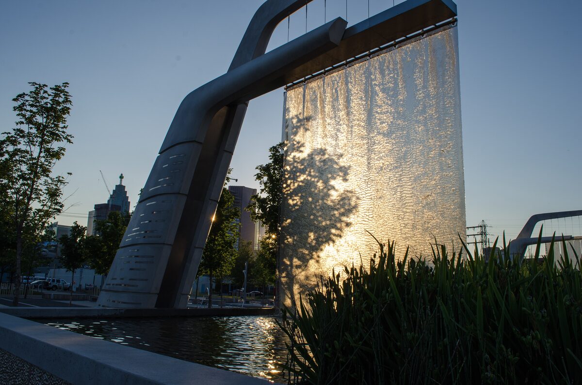 A tall sheet of falling water in a steel frame at Sherbourne Common, lit by the low evening sun