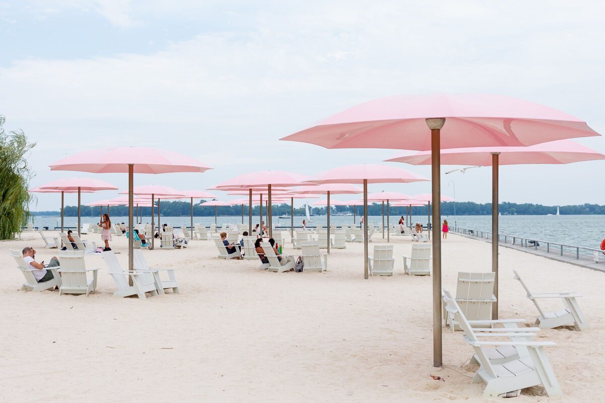 Pink umbrellas and white lounge chairs on the sand of an urban beach beside the lake