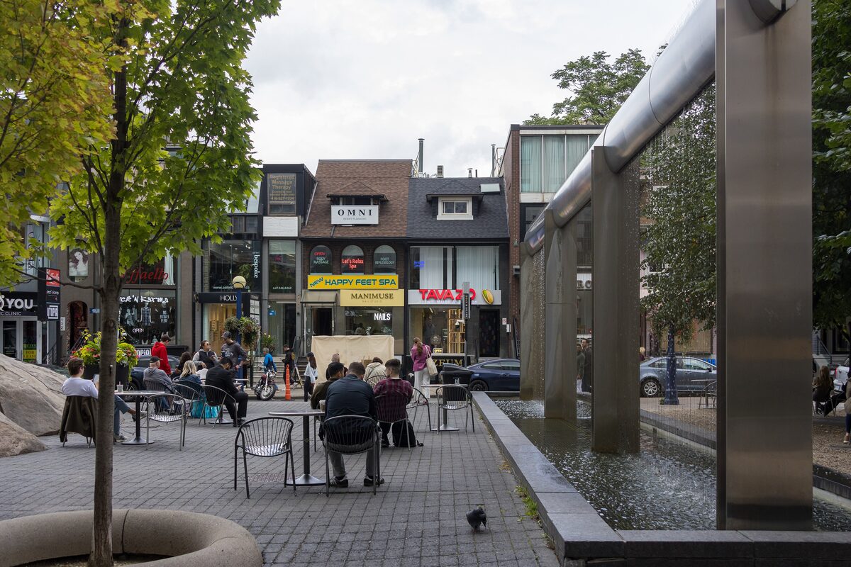 A small paved square in Yorkville with café tables, a water feature and low shopfronts behind