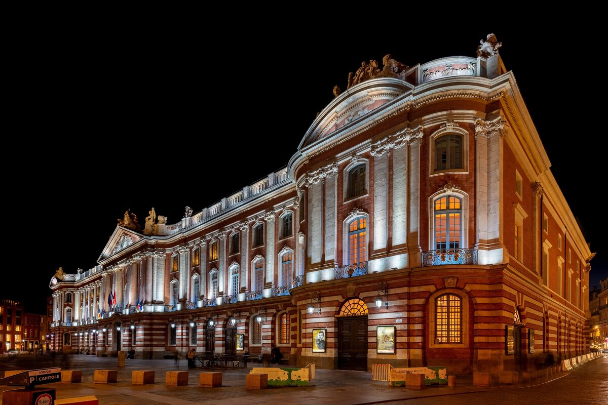 The floodlit Capitole of Toulouse at night, its pink-and-white brick facade glowing against a black sky