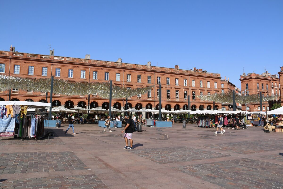 Brick arcades and market stalls along one side of Place du Capitole in Toulouse