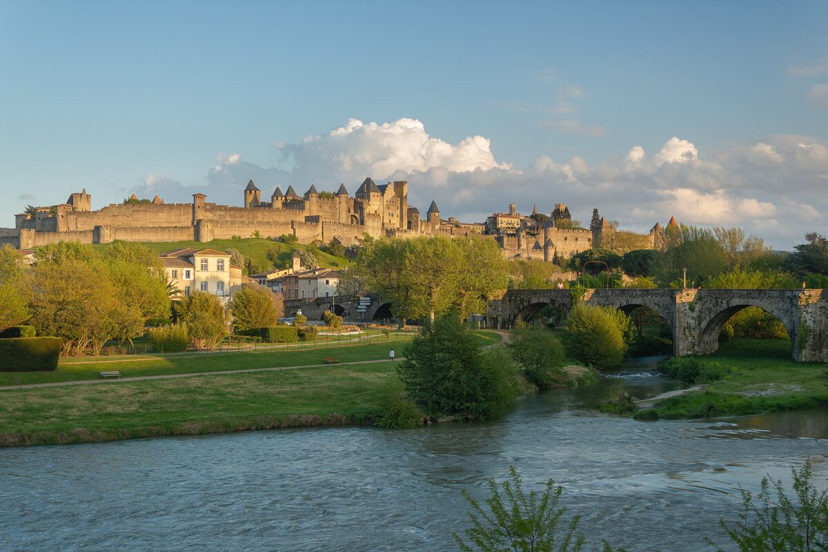 The walls and towers of the Cité de Carcassonne on their hill above the Aude, with the Pont Vieux in front in warm evening light