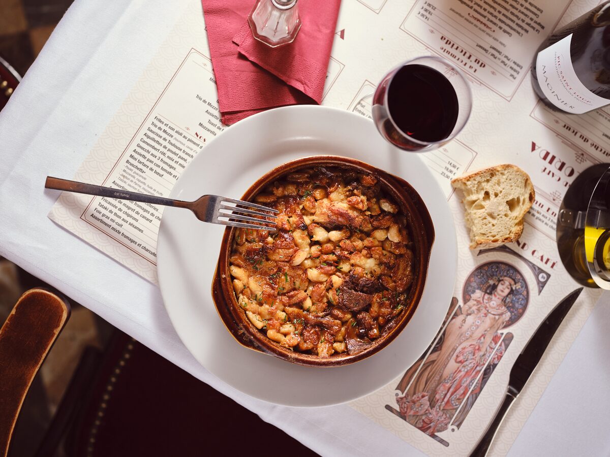 A cassoulet baked in an earthenware dish, with a browned crust of white beans, beside a glass of red wine and a piece of bread