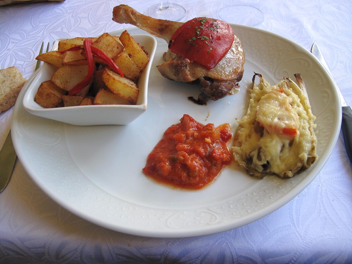A duck leg confit served with fried potatoes and a tomato sauce on a white plate