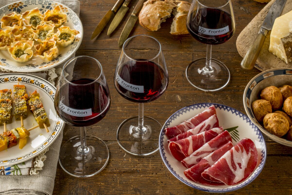 Glasses of red wine and a plate of cured meat and snacks on a wooden table