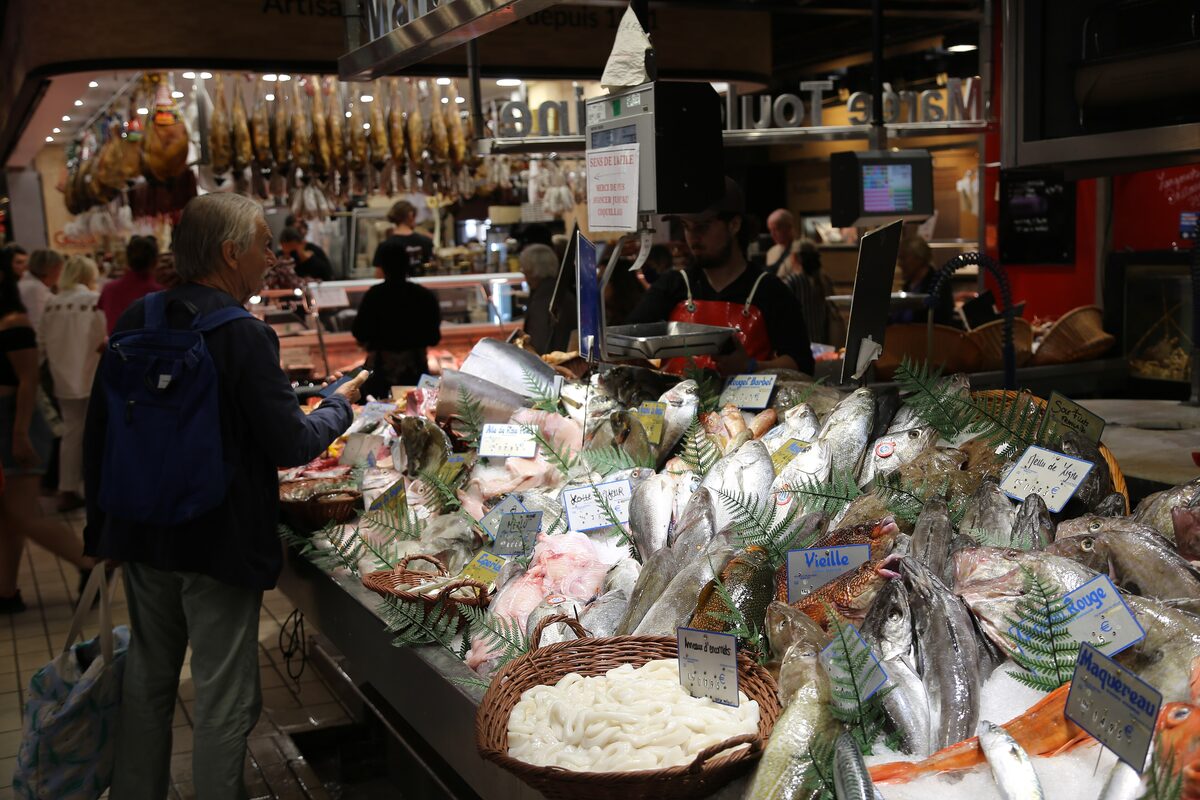 Fish and seafood on ice at a stall in the Victor Hugo market, with a shopper in the foreground
