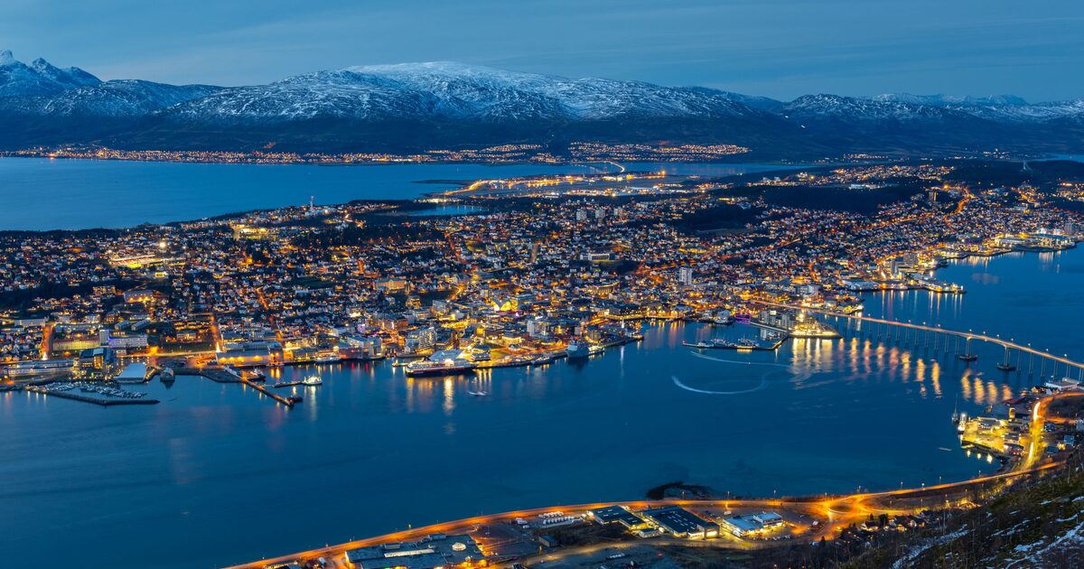 Tromsø at blue hour seen from above, with the lights of the island city, the long bridge to the mainland and snowy mountains across the fjord