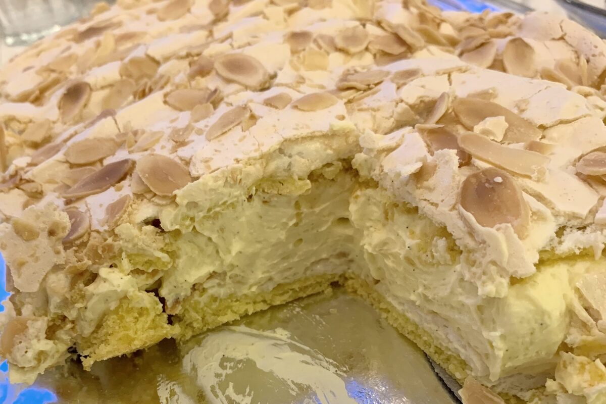 A slice of Kvæfjord cake with layers of sponge, meringue topped with almonds and vanilla cream