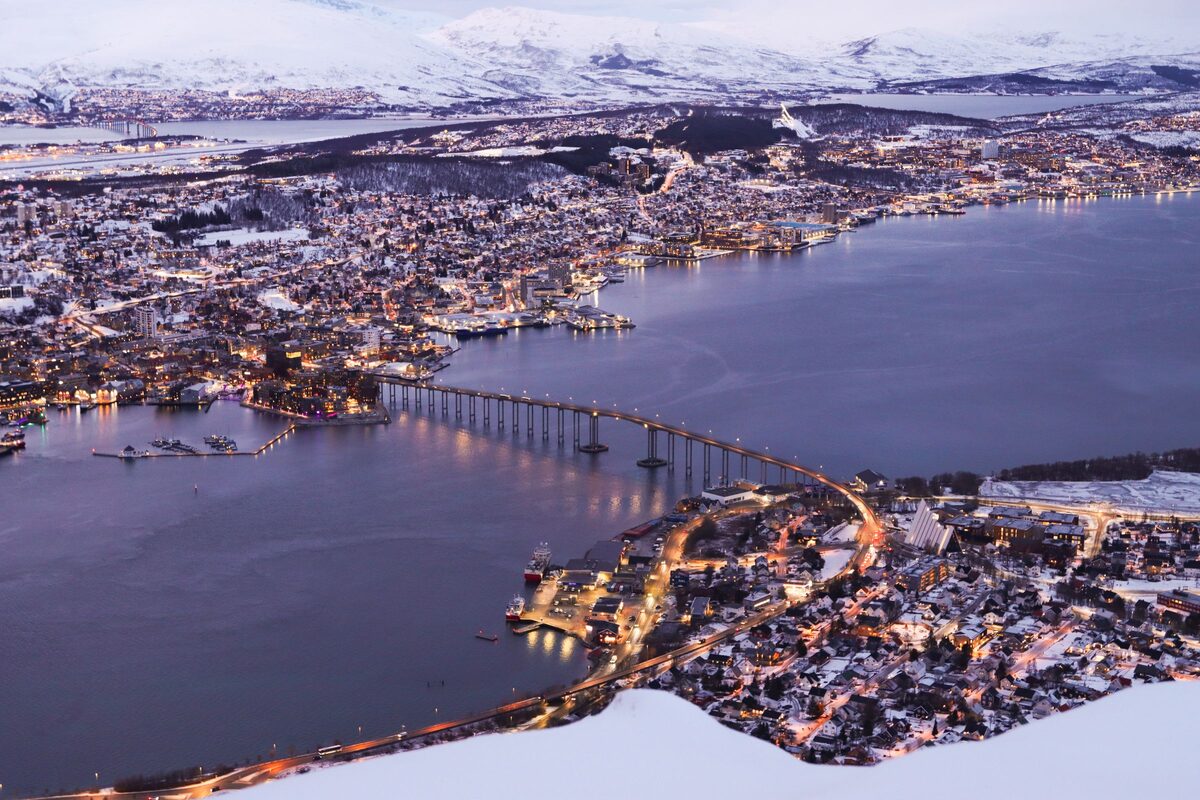 Tromsø at twilight seen from Storsteinen, with the lit-up island, the bridge and snowy mountains around the fjord