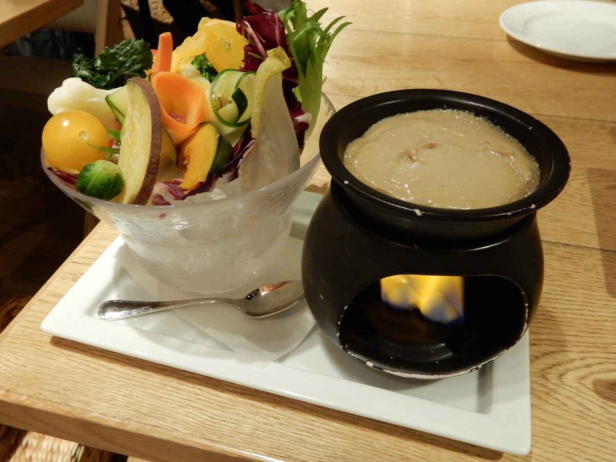 Bagna cauda over a small flame beside a glass of raw vegetables