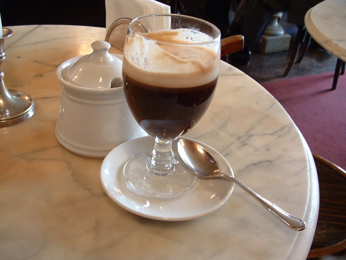 A bicerin in a glass on a marble table, dark coffee under a cream-colored foam