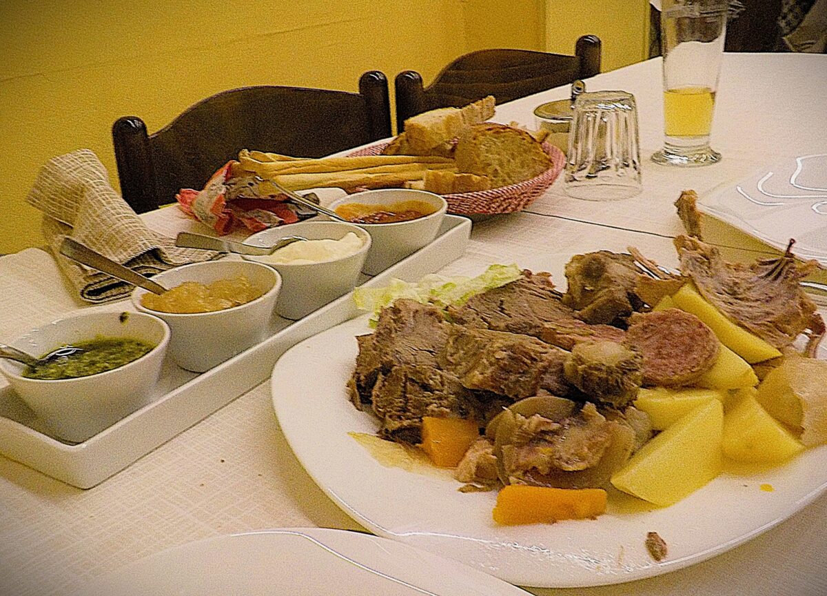 Bollito misto, boiled meats and potatoes, with bowls of sauces beside the plate