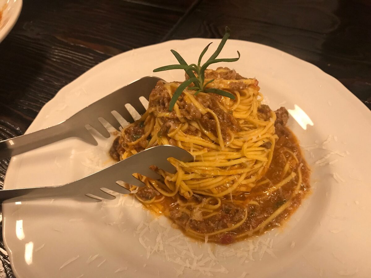 A plate of tajarin with meat ragù and a sprig of rosemary